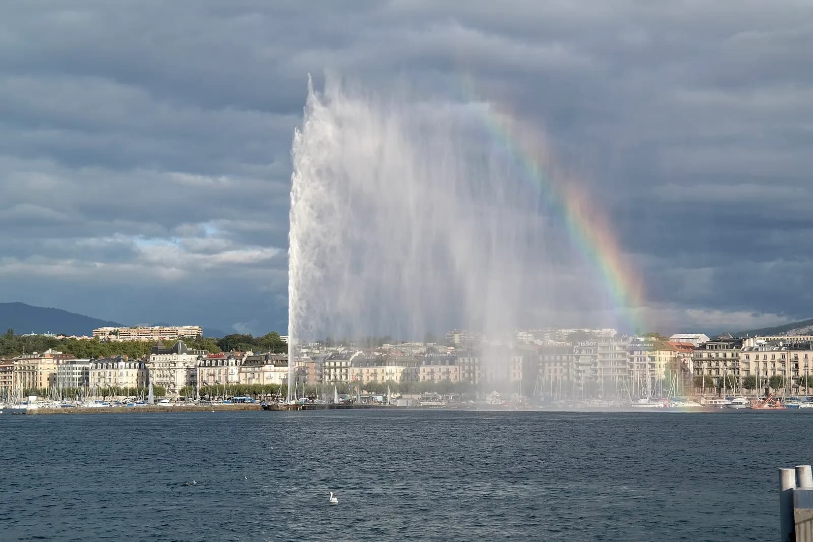 The Geneva Jet d'Eau under a rainbow, in front of the lakeside quays
